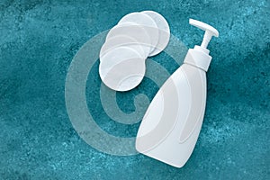 Face tonic in white dispenser bottle and many cotton discs on aqua background. Plastic bottle with liquid. Text, copy space.