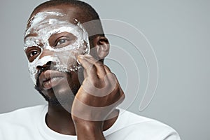 Face Treatment. Skin Care Procedure For Man. Model Applying White Facial Mask During Spa Relaxation. photo