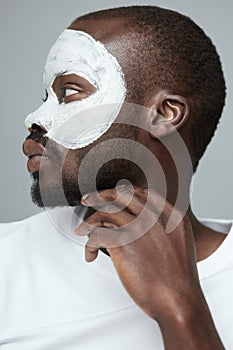 Face Treatment. Skin Care Procedure For Man. Model Applying White Facial Mask During Spa Relaxation.