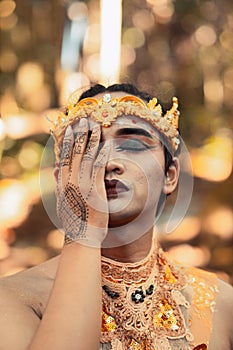 The face of a tribal king wearing a golden crown and covering his face with his hand in shirtless