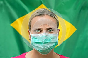 Face of a woman in a mask looking at the camera against the background of the Brazil flag. Influenza from coronavirus, prevention