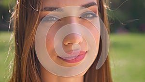 Face of woman is watching at camera in park in daytime, flirt concept, blurred background