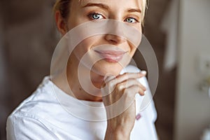 Face of young attractive Caucasian woman touching chin with hand and smiling. Portrait.
