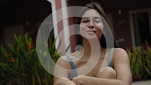 Face of a young and beautiful European brunette girl in a swimming suit close-up sitting near swimming pool touching the skin of