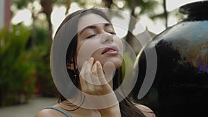 Face of a young and beautiful European brunette girl in a swimming suit close-up sitting near swimming pool touching the skin of