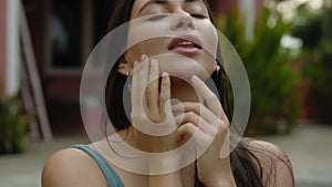 Face of a young and beautiful European brunette girl in a swimming suit close-up sitting near swimming pool touching the skin of