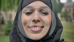 Face of young beautiful muslim girl in hijab is standing and smiling in daytime, in bad weather, watching at camera