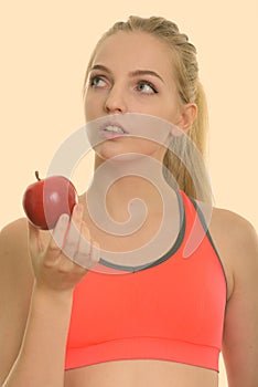 Face of young beautiful teenage girl holding red apple while thinking ready for gym