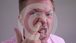 Face of young businessman picking nose in front of mirror