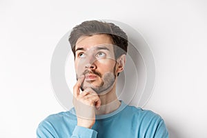 Face of young caucasian man looking up pensive, making choice or thinking, pondering while standing over white