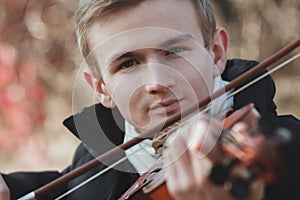 Face of a young elegant man playing the violin on autumn nature backgroung, a boy with a bowed instrument practicing, musical