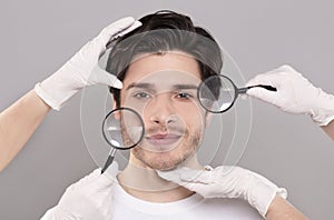 Face of young handsome man with beautician`s hands and magnifiers