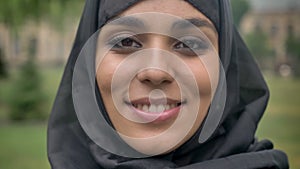 Face of young sencere muslim girl in hijab is smiling in daytime, in bad weather, watching at camera, religiuos concept