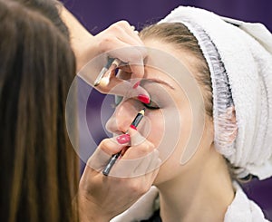 Face of young woman and makeup artist with brushes in her hands is applying makeup