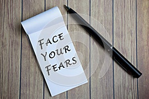 Face your fears text on notepad with a pen on a wooden desk.