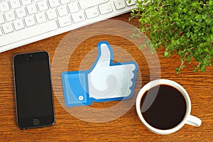 Facebook thumbs up sign placed on wooden background with coffee, keyboard and smart phone