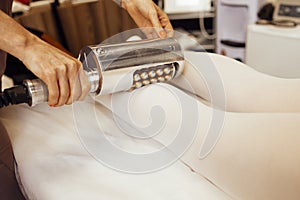 Faceless beautician using massager to remove fat from hips of anonymous customer