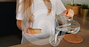 Faceless girl in kitchen open jar with cork cap pour water glass drink