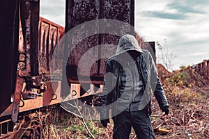 Faceless hooded homeless man among old obsolete freight train wagons photo