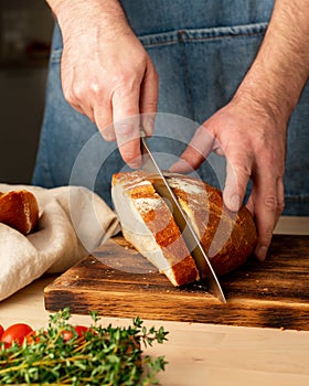 Faceless man cutting fresh home baked crusty bread with large knife