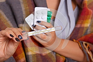 Faceless picture of sick girl, persone being treated for cold at home in warm checkered plaid, woman`s hand holding thermommeter photo