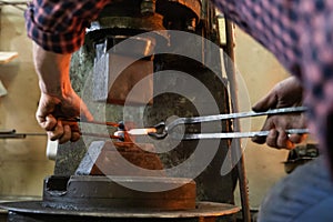 Crop blacksmith pressing hot metal stick in grungy smithy