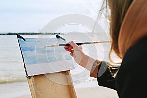 Faceless shot of a female drawing on a beach. en plein air artist