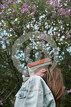Faceless shot of female holding a book on her face outdoors