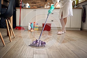 Faceless shot of houswife moping floor in the kitchen, with chemical bottles in the background