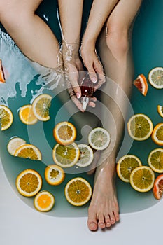 Faceless shot of woman in a bathroom filled with blue water and various cut citrus fruits holding serum in her hands