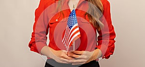 Faceless shot of a woman wearing red shirt holding USA flag with both hands.