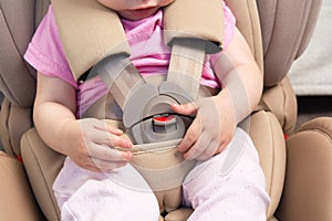 Faceless small baby sitting in special car seat with safety seatbelts