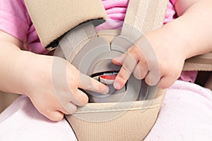 Faceless small baby sitting in special car seat with safety seatbelts