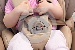 Faceless small baby sitting in special car seat with safety seatbelts