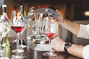 Faceless sommelier pours red wine into stem glass.