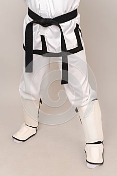 Faceless vertical studio shot of male legs wearing shin guards and black belt.