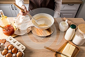 A faceless woman holds a ladle of cooked liquid pancake dough over a bowl. kitchen countertop with ingredients for further cooking