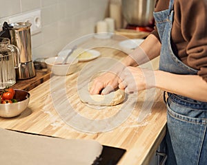 Faceless woman kneading dough on kitchen table at home, apartment. Homemade food