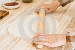 Faceless woman roll out dough with rolling pin on kitchen table at home,