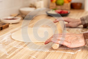 Faceless woman roll out dough with rolling pin on kitchen table at home,