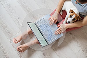 Faceless woman working from home. Unrecognizable girl sitting on the floor with a puppy of Jack Russell Terrier in his photo