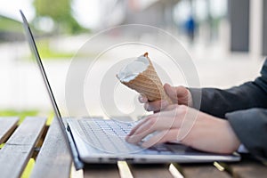 A faceless woman works at a computer on a summer terrace and eats vanilla ice cream. Close-up of female hands typing on