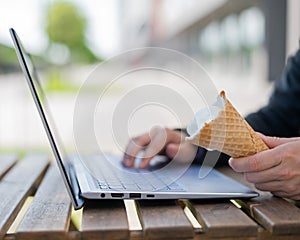 A faceless woman works at a computer on a summer terrace and eats vanilla ice cream. Close-up of female hands typing on