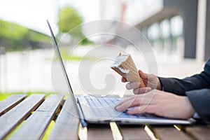 A faceless woman works at a computer on a summer terrace and eats vanilla ice cream. Close-up of female hands typing on