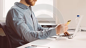 Faceless young man with credit card in hand shopping online on laptop