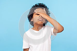 Facepalm. Portrait of forgetful upset little boy with curls covering face with hand and expressing sorrow