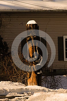 Faces of a totem pole in the dawn sunlight with snow atop