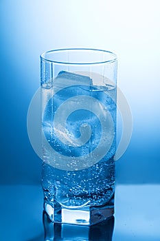 Faceted glass with pure water and ice on the blue background