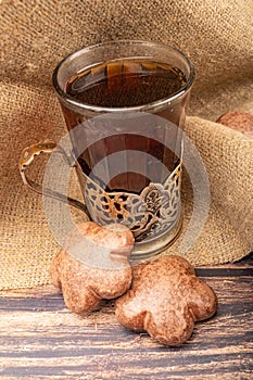 A faceted glass of tea in a vintage Cup holder and chocolate gingerbread on a background of rough homespun fabric. Close up