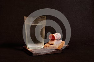 Faceted glass of vodka, sandwich with rye bread, herring, ham